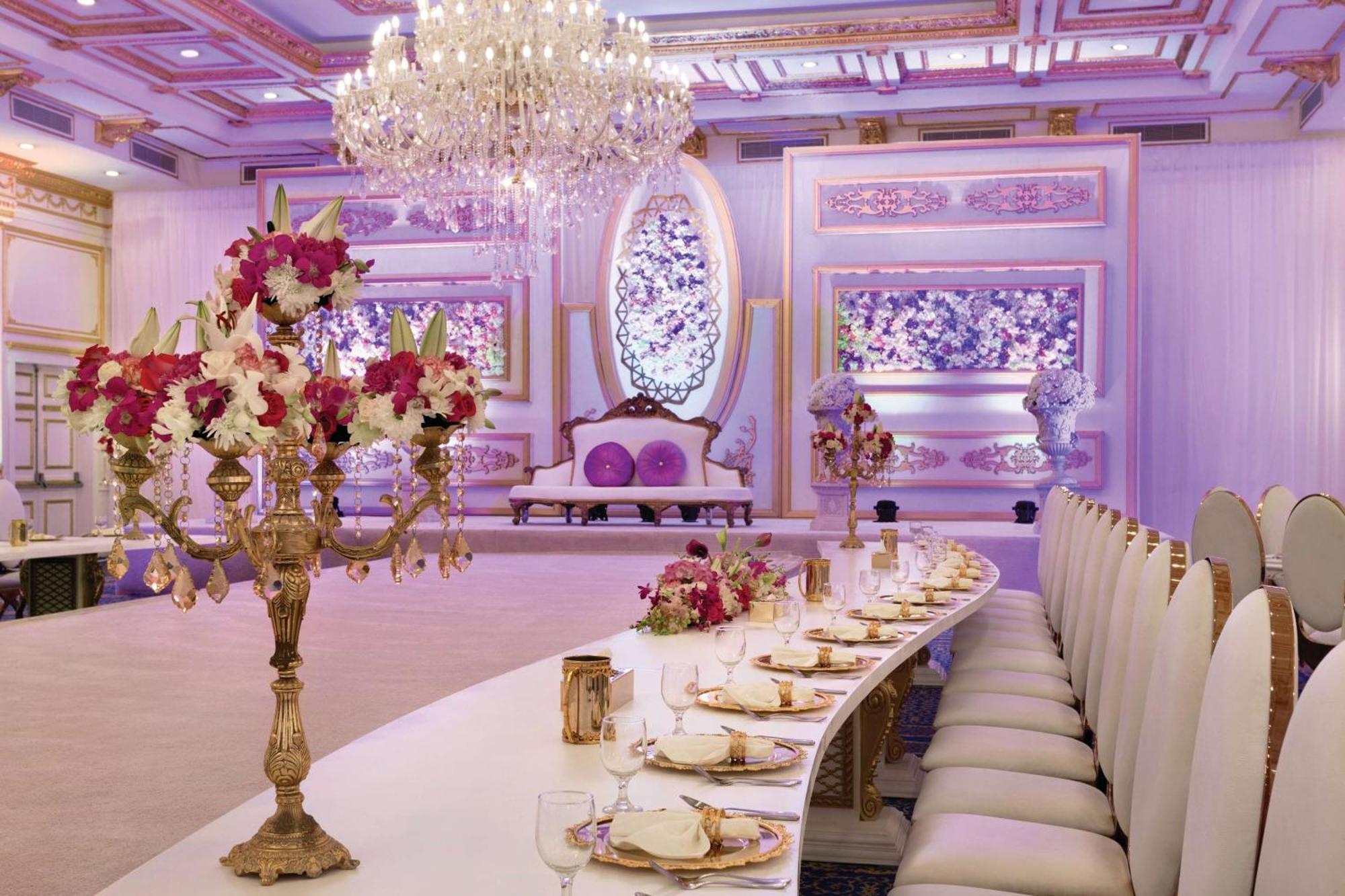 Grand Regency Doha, Trademark Collection By Wyndham Zewnętrze zdjęcie The photo displays an elegantly decorated banquet or dining hall. It features a long, curved table set for a formal event, with fine china and floral centerpieces. Luxurious decorations include a grand chandelier hanging from the ceiling, and the wal