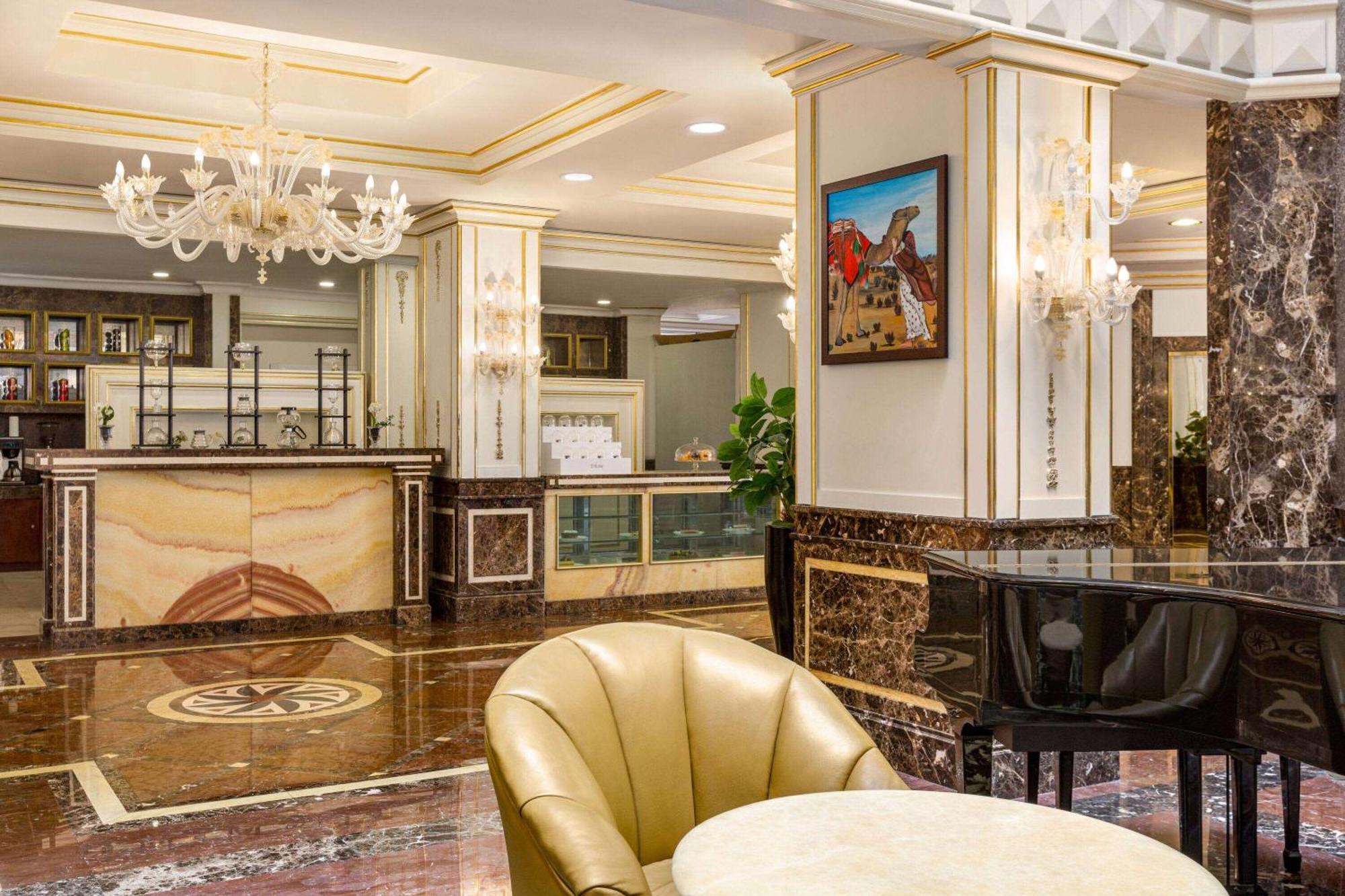 Grand Regency Doha, Trademark Collection By Wyndham Zewnętrze zdjęcie The photo depicts an elegant hotel lobby interior. It features a polished marble floor with intricate patterns. In the background, there is a reception desk made of marble and wood, with decorative elements and a glass display. On the walls, you can 