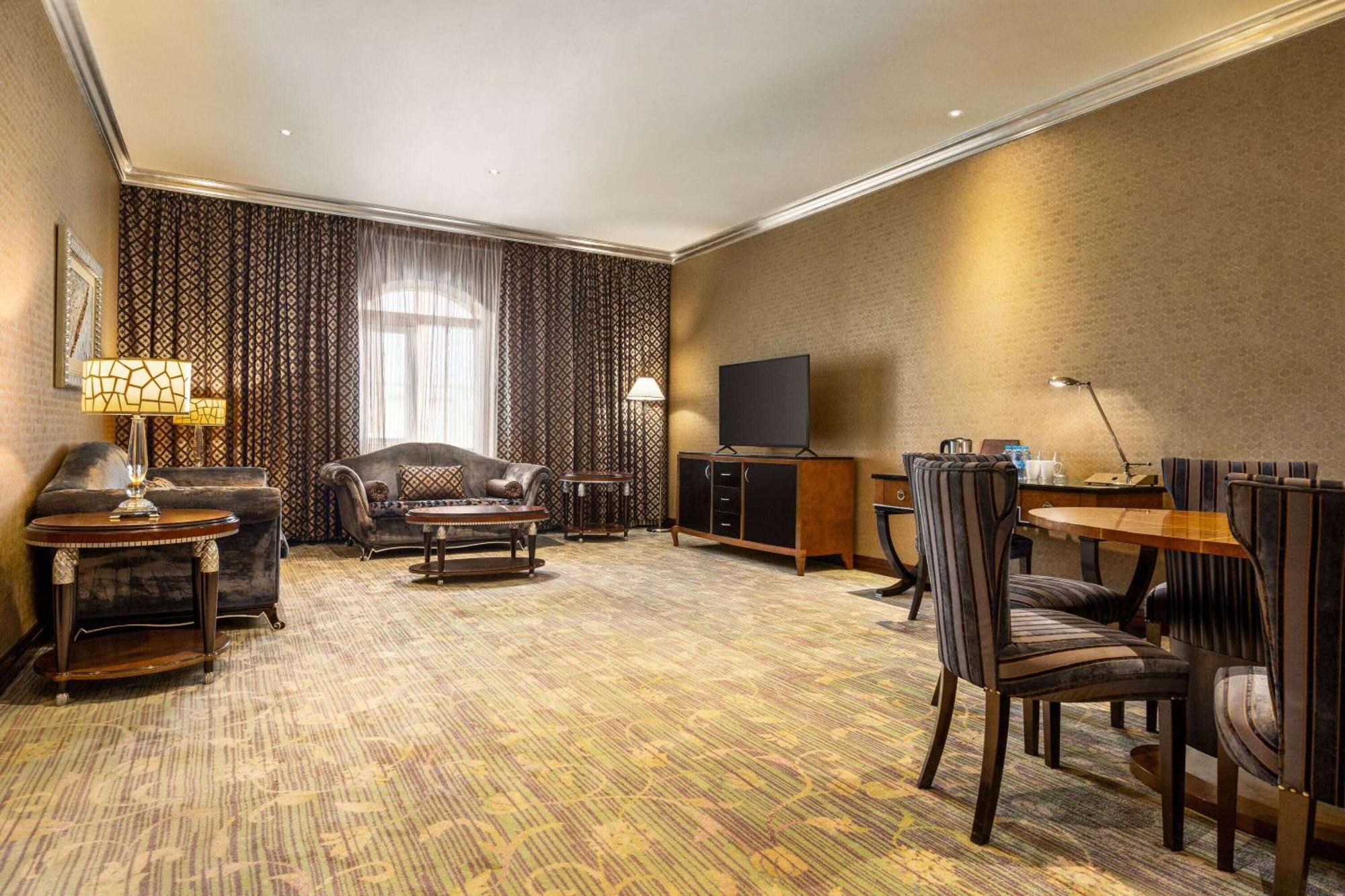 Grand Regency Doha, Trademark Collection By Wyndham Zewnętrze zdjęcie The photo shows a spacious lounge or living area. It features a comfortable seating arrangement with a dark-colored sofa and armchairs, arranged around a coffee table. There's a dining table with matching chairs, suggesting it can accommodate meals o